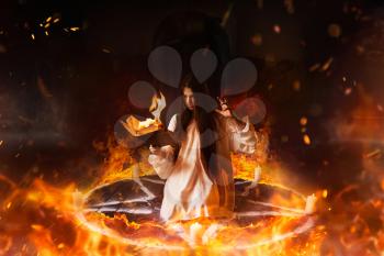 Young woman in white shirt sitting in the center of burning pentagram circle and reads spellbook, gark magic ritual, mysticism