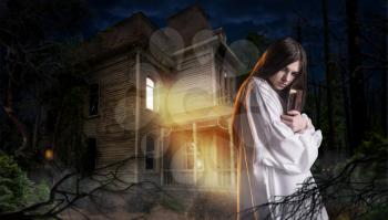 Young woman with spellbook in hand against abondoned house in the night. Dark magic, occultism and exorcism