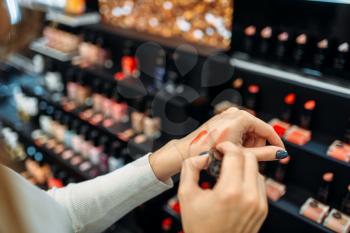 Female customer testing lipstick in the make-up shop. Cosmetics choosing in beauty store, make-up salon