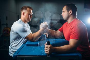 Two arm wrestlers fighting on their hands at the table with pins, the dust from the talc in the air, wrestling competition. Wrestle challenge, power sport of muscular men