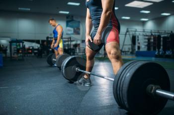 Two strong weightlifters doing exercise with barbells, gym interior on background. Weightlifting workout in fitness club, bodybuilding