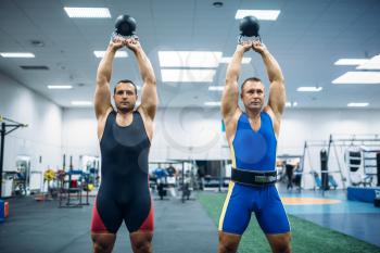Two male lifters lifted kettlebells over thier heads, lifting training in gym. Weightlifting workout in sport or fitness club