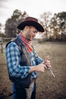Cowboy checks his revolver before gunfight on ranch, western. Vintage male person with gun on farm, wild west adventure