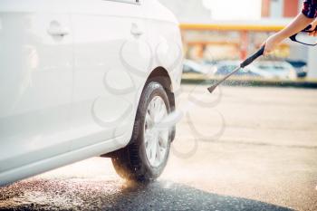 Female person cleans car wheels with high pressure water gun. Young woman on self-service automobile wash. Outdoor vehicle washing at summer day 