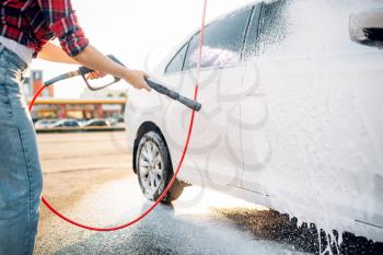 Female person with high pressure water gun in hands wash off the foam from the car. Young woman on self-service automobile washing. Outdoor vehicle cleaning at summer day 