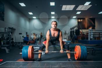 Male weightlifter prepares to pull heavy barbell, deadlift, gym interior on background. Weightlifting workout in sport or fitness club, bodybuilding