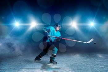 Hockey player with stick and puck makes a throw, ice arena, spotlights on background