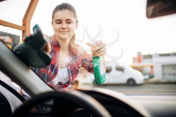 Woman cleans the windshield of the car with spray, view from the inside, carwash. Lady on self-service automobile washing. Outdoor vehicle cleaning at summer day 