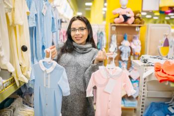 Woman choosing clothes in the store for newborns. Future mother in shop of goods for infants