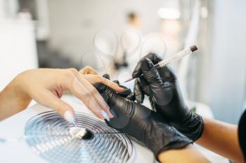 Beautician in black gloves sticks the nails of the client, manicure in salon. Manicurist doing hands care cosmetic procedure