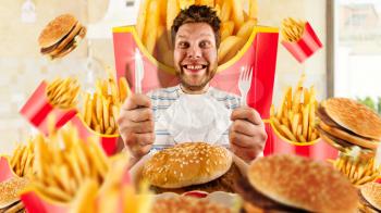 Fast food concept, man and burgers with fries. Crazy male person with knife and fork prepares to eating