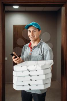 Pizza delivery boy in t-shirt and cap calls to customer, delivering service. Courier from pizzeria holds cardboard packages and phone
