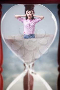 Sad woman stands inside an hourglass closeup, deadline concept
