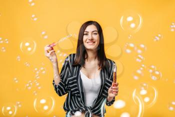 Young woman blows soap bubble, yellow background. Female person blowing colorful balloons