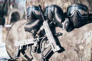 Paintball masks with protection glasses and marker guns, nobody. Extreme game equipment, sport ammunition