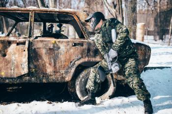 Paintball battle around burned car in winter forest, paintballing. Extreme sport, military game