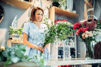 Female florist holds fresh flowers in floral shop. Floristry business, bouquet making 