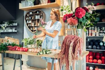 Female floral artist sorts fresh flowers on the table in shop.  Florist making bouquet at the workplace in boutique