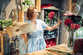 Female florist decorates composition with birch bark on the table in flower shop. Floral artist making bouquet at the workplace