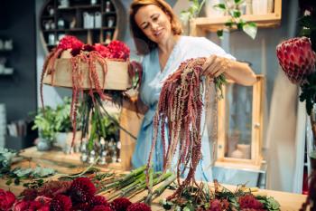 Female florist decorates with bunch flower bouquet in shop closeup. Floral artist making composition at the workplace