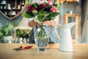 Female florist puts fresh flower bouquet into a vase in floral shop. Floristry service, floristic business