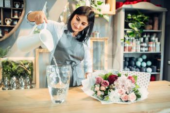 Female florist pours water into a vase in flower boutique. Floristry service, floristic business, floral shop
