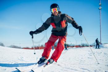 Skier in helmet and glasses riding from speed slope, front view. Winter active sport, extreme lifestyle. Downhill skiing