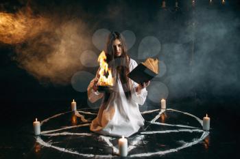 Witch in white shirt sitting in the center of pentagram circle with candles, dark magic ritual process. Occultism and exorcism