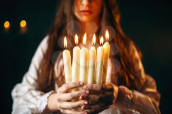 Female person in white shirt holds candles in hands. Dark magic ritual, occultism and exorcism, divination