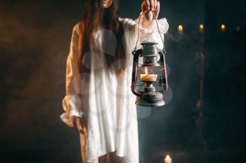 Female person in white shirt holds kerosene lamp in hand. Dark magic ritual, occult and exorcism