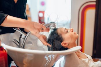 Hairdresser washes customer hair in basin, hairdressing salon. Professional haircutting in a beauty studio