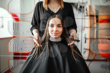 Woman in hairdressing salon, female stylist with scissors and comb in hands on background. Hairstyle making in beauty studio