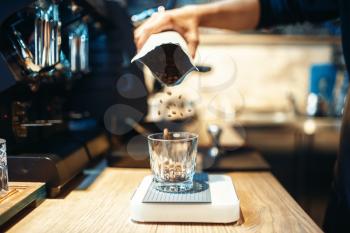 Barista hand pours coffee beans into the glass, cafe counter on background. Professional espresso preparation by bartender in cafeteria