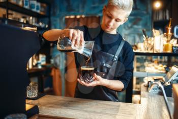 Young male barista in apron makes fresh black coffee at cafe counter. Barman works in cafeteria, bartender prepares espresso