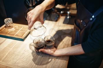 Young male barista makes fresh black coffee at cafe counter. Barman works in cafeteria, bartender prepares espresso