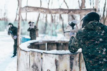 Paintball player shooting at the enemy team, winter forest battle. Extreme military game
