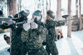 Paintball players in uniform and masks poses with marker guns in hands after winter forest battle. Extreme sport game