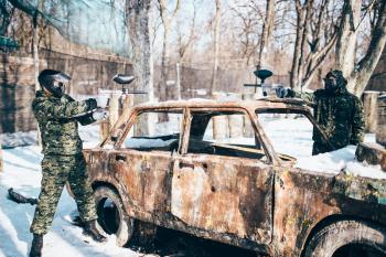 Paintball battle, players shoots because of burned car in winter forest, paintballing. Extreme sport, military game