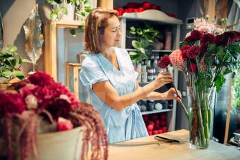 Female florist puts fresh flowers in a vase in floral shop. Floristry service, floristic business