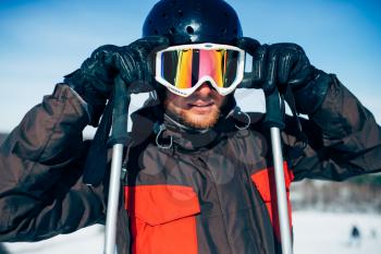 Male skier in helmet puts on glasses, front view. Winter active sport, extreme lifestyle. Downhill skiing