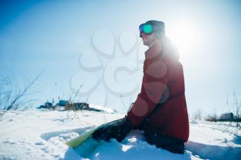Snowboarder in glasses sitting on snowy slope in sunny day. Winter extreme sport, active lifestyle. Snowboarding in mountains