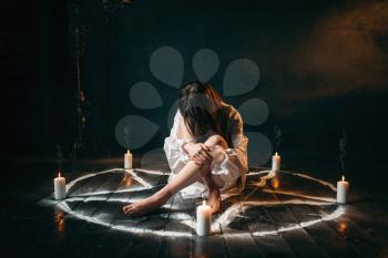 Female person in white shirt sitting in pentagram circle with candles. Dark magic ritual, occultism