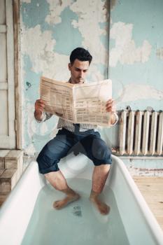 Funny businessman sitting on the edge of the bathtub and reads newspaper.