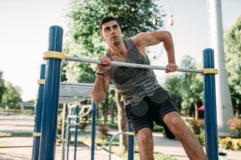 Athletic man doing exercise on horizontal bar on outdoor fitness workout. Strong sportsman on sport training in park
