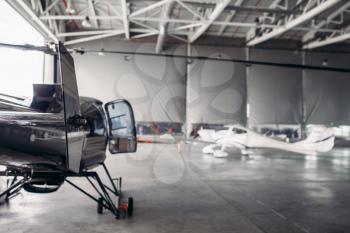 Private airline air park in airport hangar, small turboprop airplane and helicopter in aerodrome building, propeller plane and copter, inspection before flight.Business air transportation or aeroclub