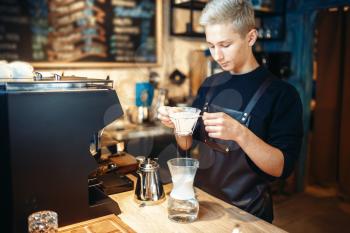 Young male barista makes coffee at the counter. Espresso machine on background. Barman works in cafeteria, bartender occupation