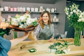 Florist gives fresh bouquet to female customer in flower boutique. Floral shop interior on background