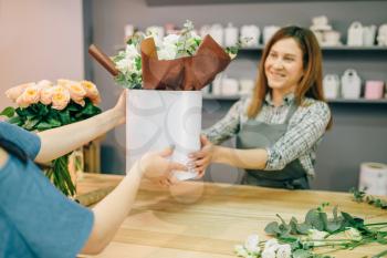 Florist gives fresh flower composition in vase to female customer in flower boutique. Floral shop interior on background