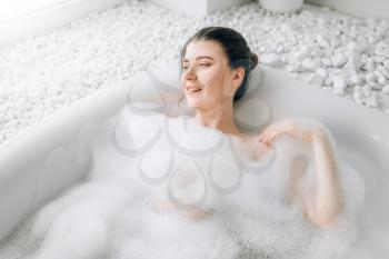 Attractive lady lying in bath with foam, top view. Relaxation, health and skin care in bathroom, spa