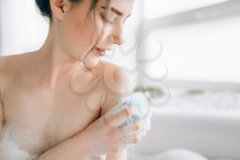 Female person soaps the body with a sponge in bath closeup. Bodycare and skincare in bathroom